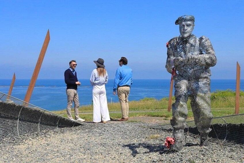 Una scultura di un soldato su una spiaggia, con una recinzione e vista sull'oceano. 3