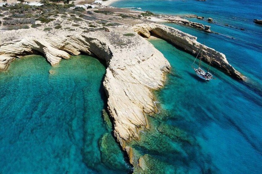A coastal landscape with a rocky formation, clear turquoise waters, and a sailboat anchored near the shore. 5