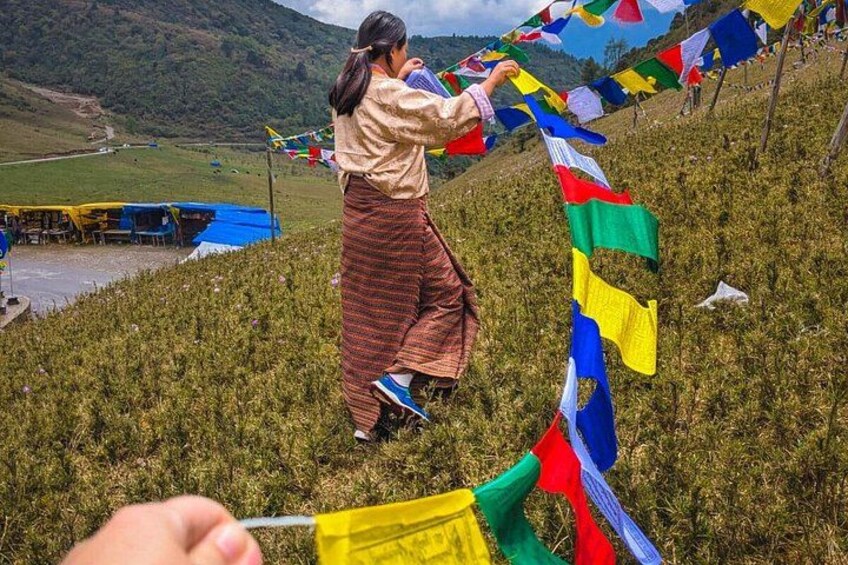 A person tying colorful prayer flags on a grassy hillside. 5