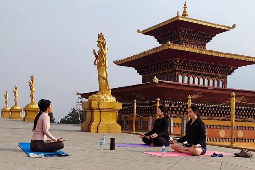 People meditating on mats in front of a temple with golden statues and a pagoda. 3