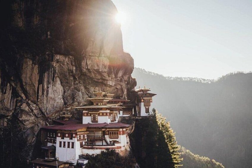 A monastery perched on a cliffside with a mountain backdrop. 1