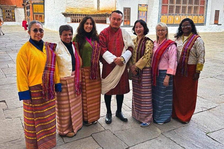 A group of people in traditional attire standing in a courtyard with a building in the background. 4