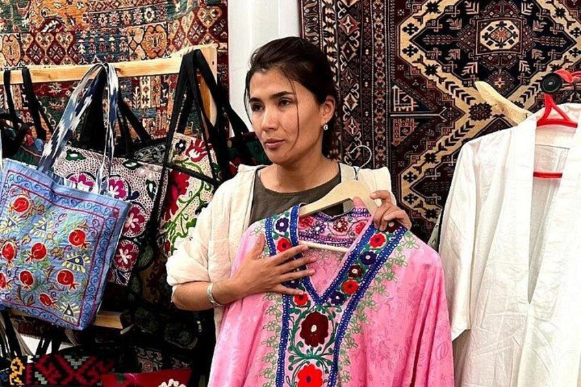 A person holding a pink garment with embroidery, standing in front of a display of patterned bags. 5