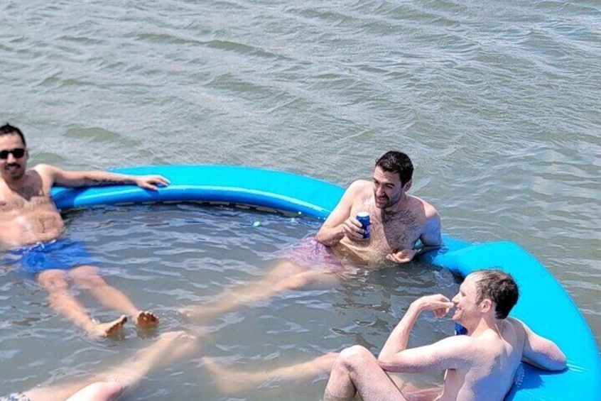 Three people in a blue inflatable pool floating on water. 5