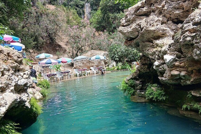 A clear blue pool surrounded by rocky terrain, with several umbrellas and chairs indicating a recreational area. 2
