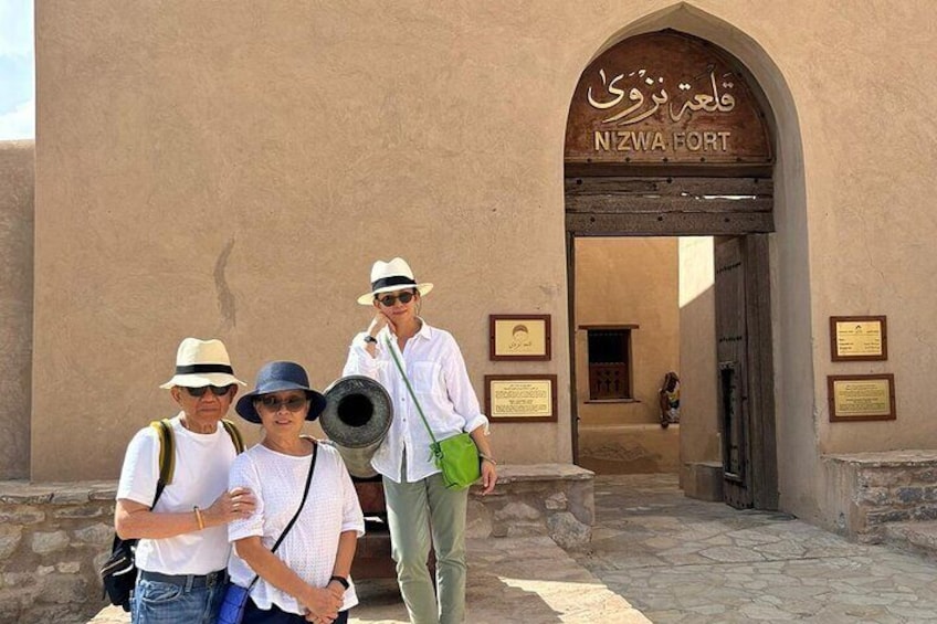 Un groupe de personnes se tient devant un bâtiment sur lequel on peut lire l’inscription « FORTERESSE DE NIZWA ». 1
