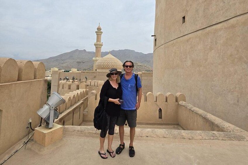 Un uomo e una donna in piedi su un tetto, con vista su una moschea e montagne sullo sfondo. 3