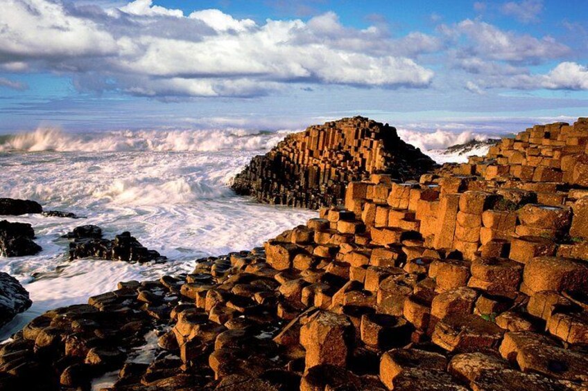 A coastal landscape with stacked stone structures and waves crashing against the shore. 2
