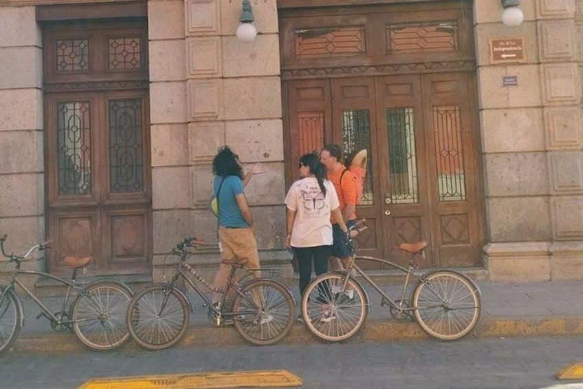 Un grupo de personas de pie junto a bicicletas frente a un edificio con puertas ornamentales. 4