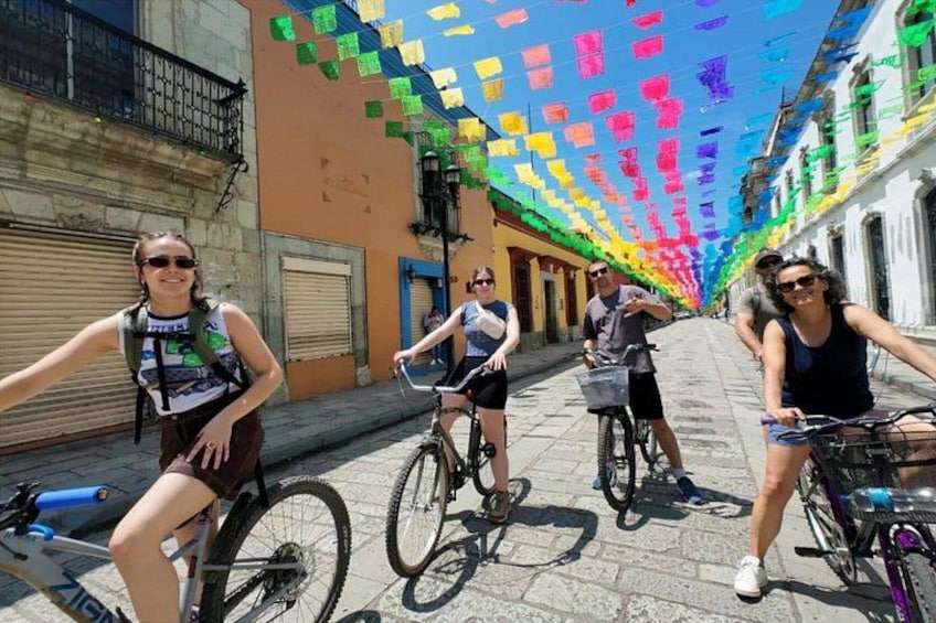 Una calle con ciclistas, decoraciones colgantes coloridas y edificios. 1