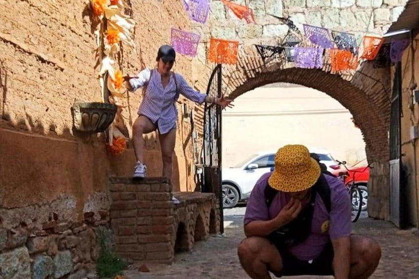Un callejón estrecho con un arco de ladrillo, una persona agachada con sombrero y otra de pie en un escalón. 5