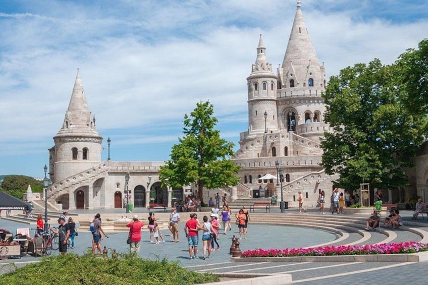 Ein historisches Gebäude mit zwei Türmen, einem Platz mit Menschen und einem Blumenbeet. 1