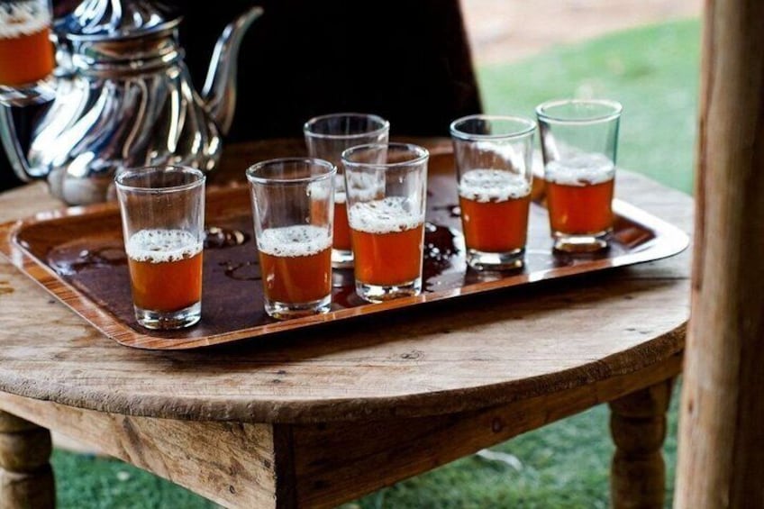 A tray with six glasses of tea on a wooden table outdoors. 3