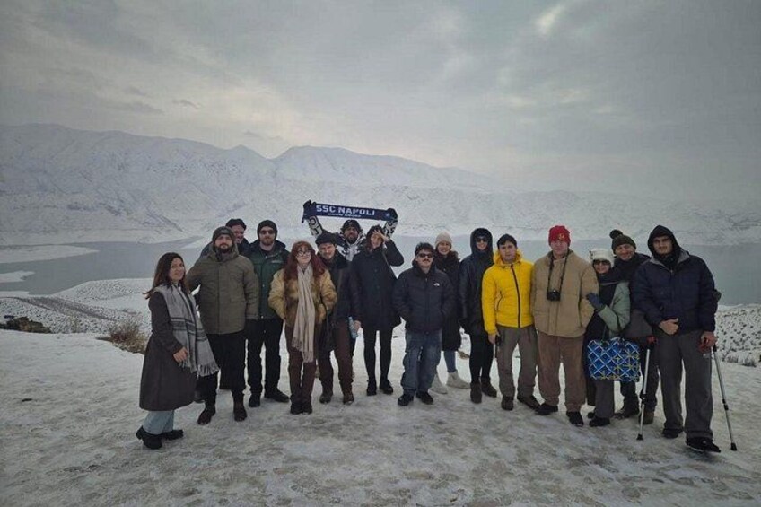 Un gruppo di persone in piedi su una montagna innevata, con un lago sullo sfondo. 5