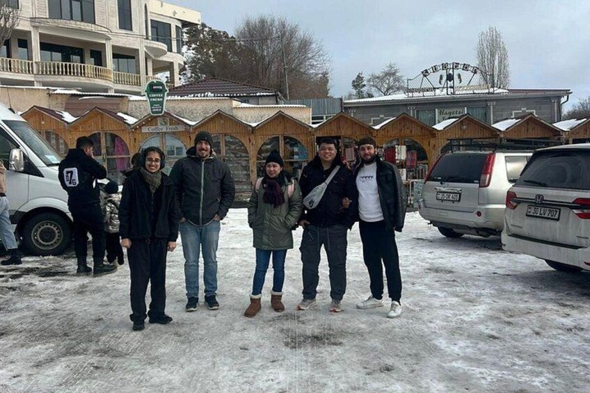 Un gruppo di persone in un parcheggio innevato, con edifici in legno sullo sfondo. 3