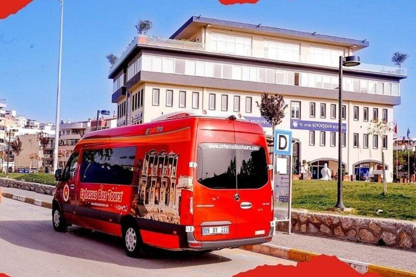 En röd buss med texten ”Ephesus Bus Tours” på sidan, parkerad framför en byggnad med en skylt som lyder ”TILL JOHANNES DÖPARENS BRUNNAR”. 4