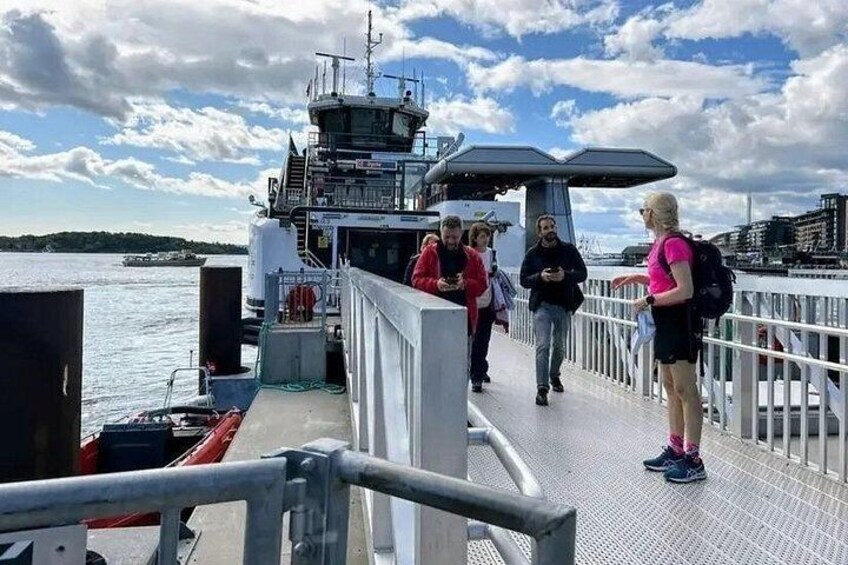 A ferry dock with people walking, a bridge, and a body of water in the background. 5
