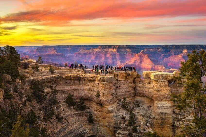 En grupp människor som står på en utsiktsplattform vid Grand Canyon under solnedgången. 1