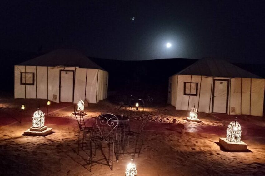 A yurt camp at night with illuminated structures and a full moon in the sky. 5