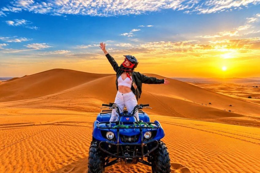 A person on a quad bike in a desert with sand dunes and a sunset. 2