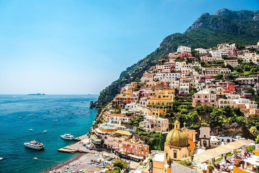 A coastal town with colorful buildings, a beach, boats, and a mountain in the background. 3