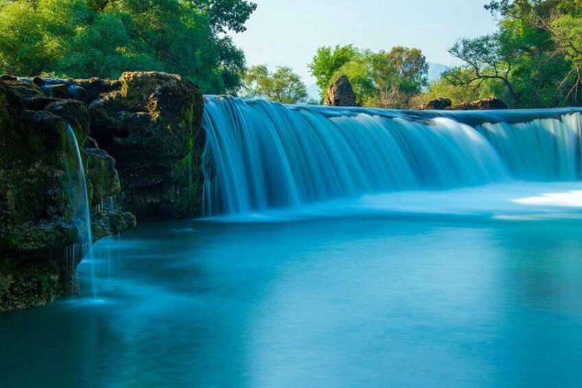 A waterfall cascading over rocks into a calm pool surrounded by lush greenery. 5