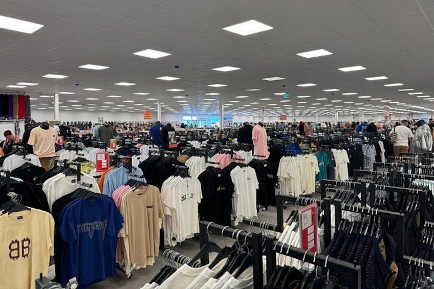 A clothing store with racks of clothes and shoppers browsing. 1