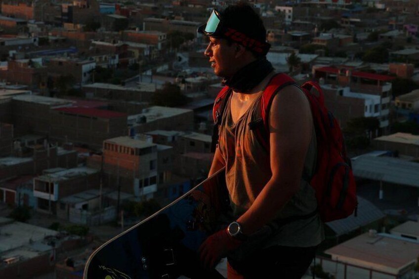 A person with a backpack and a skateboard, overlooking a densely packed urban area with various buildings. 2