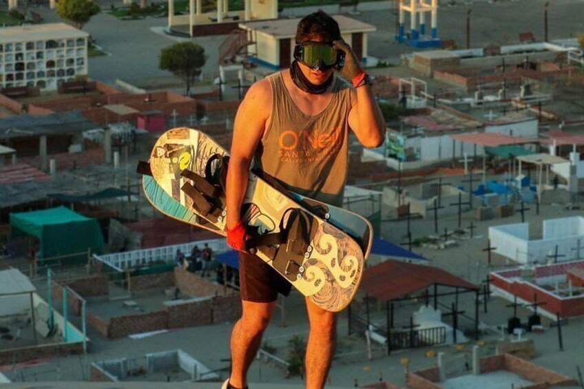 A person holding a snowboard with a patterned design, standing on a rooftop with a cityscape in the background. 3