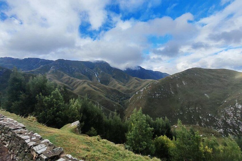 A mountainous landscape with a stone wall, green vegetation, and a clear sky. 5
