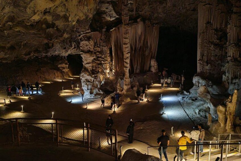 A cave with stalactites and stalagmites, illuminated by artificial lighting, with people walking around. 3