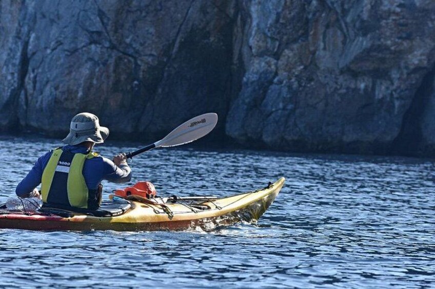 Una persona practica kayak en aguas tranquilas con acantilados rocosos al fondo. 5