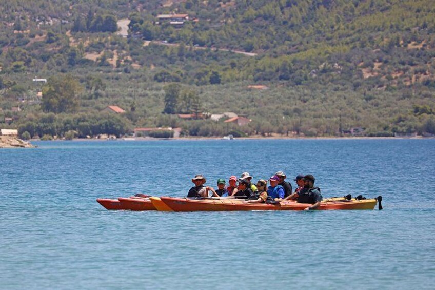 Un grupo de personas remando en un bote largo y estrecho sobre aguas tranquilas, con un paisaje montañoso al fondo. 3