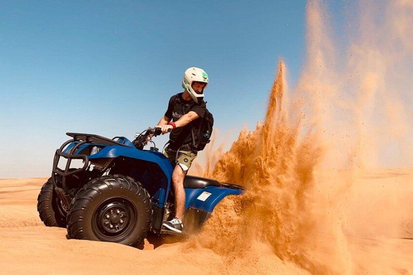 Eine Person fährt mit einem blauen Geländefahrzeug durch eine Wüste, während Sand aufwirbelt. 1