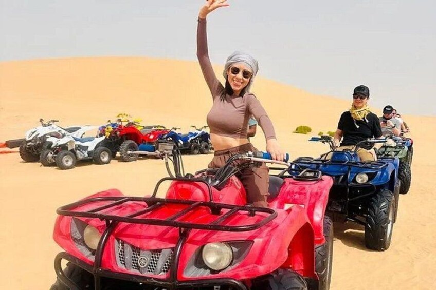 Eine Person fährt mit einem roten Quad durch eine Wüstenlandschaft, im Hintergrund sind Sanddünen und weitere Quads zu sehen. 4