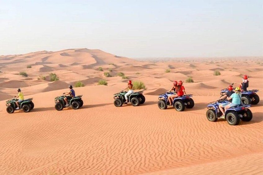 Eine Gruppe von Menschen fährt mit Quads durch eine Wüstenlandschaft mit Sanddünen. 5