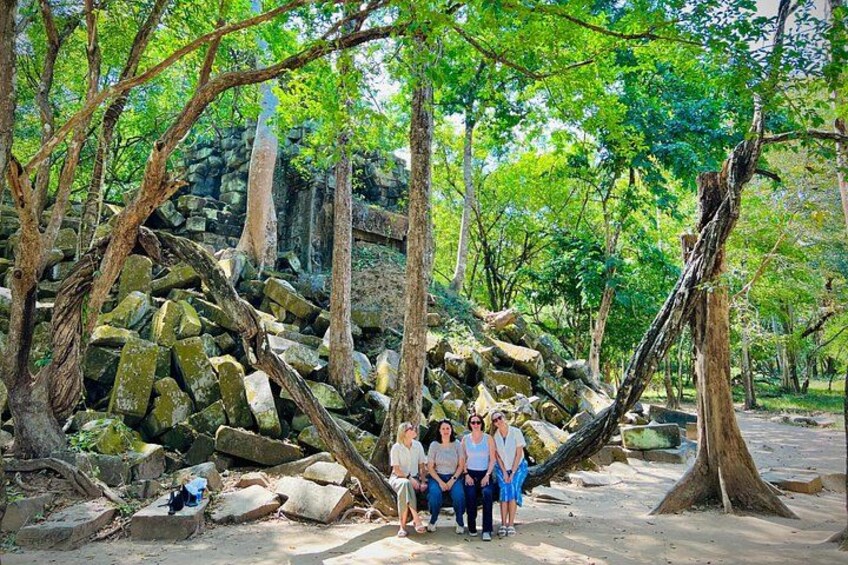 A group of people standing near a pile of rocks in a forested area with trees and a stone structure in the background. 3