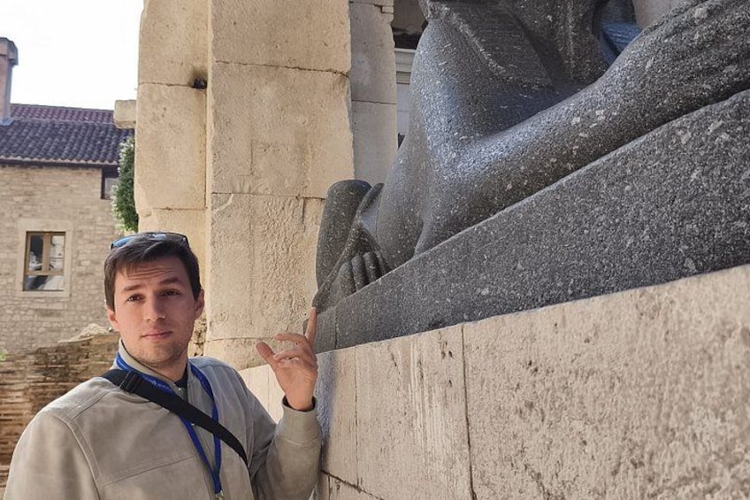 Une personne se tient à côté d’une sculpture en pierre et fait un geste avec la main. 3