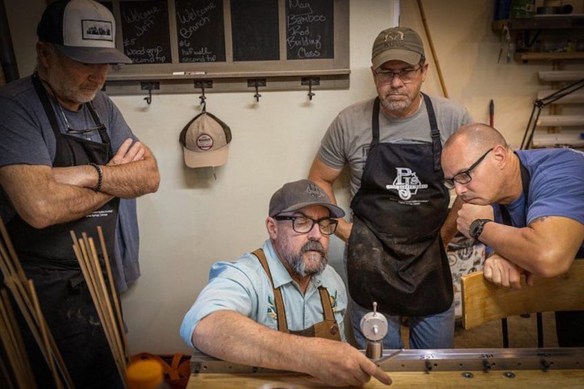 Four men in aprons working at a table with tools and a wooden box. 5