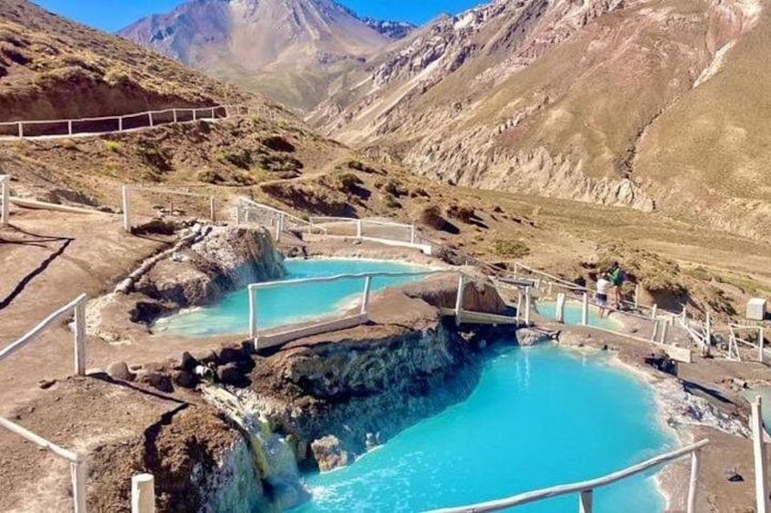 Zona de aguas termales con varias piscinas rodeadas de terreno rocoso y montañas al fondo. 1