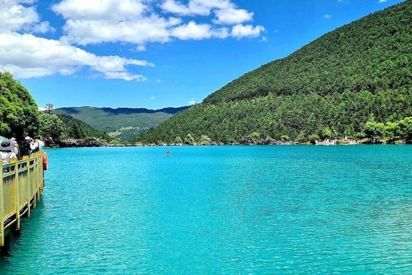 A turquoise lake surrounded by lush green hills, a wooden pier, and a clear blue sky. 5