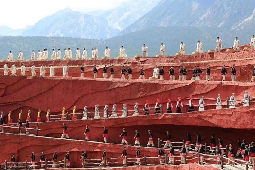 A group of people in traditional attire on a red rock formation with a mountainous backdrop. 4