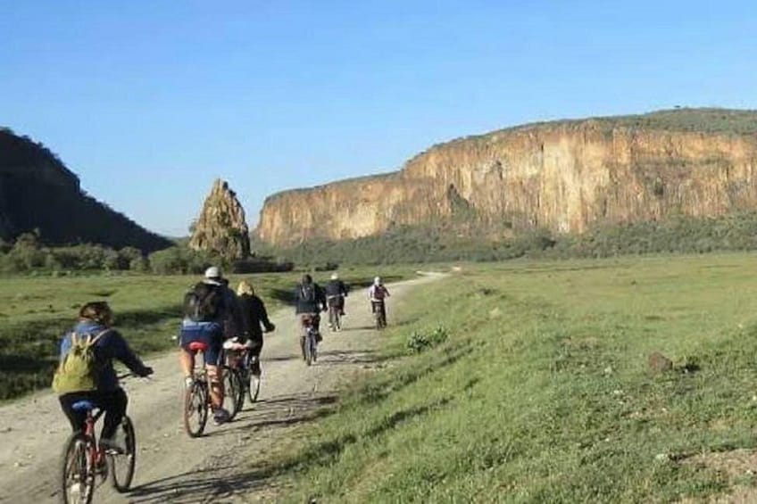Un grupo de ciclistas en un sendero de tierra con una gran formación rocosa al fondo. 5