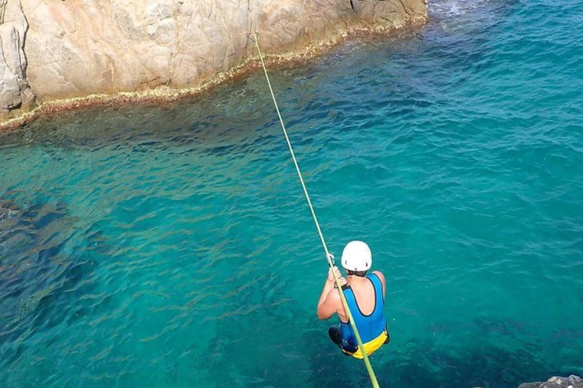 Una persona haciendo rappel hacia aguas turquesas y transparentes cerca de una costa rocosa. 4