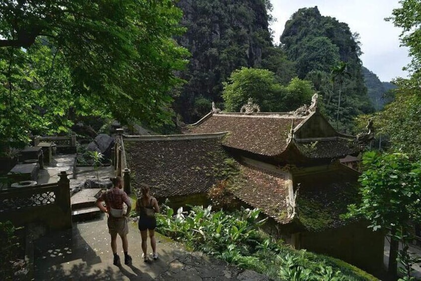 Ein traditionelles Gebäude mit Ziegeldach, umgeben von üppiger Vegetation und einer felsigen Landschaft. 1