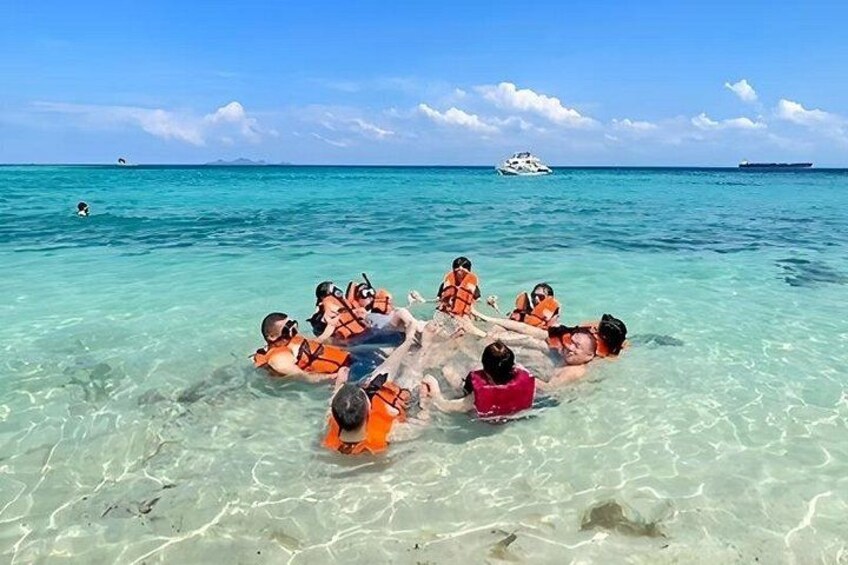 Personas nadando en aguas turquesas cristalinas, con chalecos salvavidas, y un barco y un buque en el fondo. 3