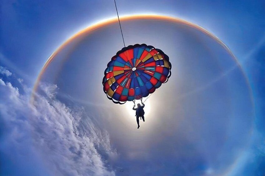 Una persona haciendo paracaidismo con un paracaídas de colores frente a un cielo con un arcoíris. 1