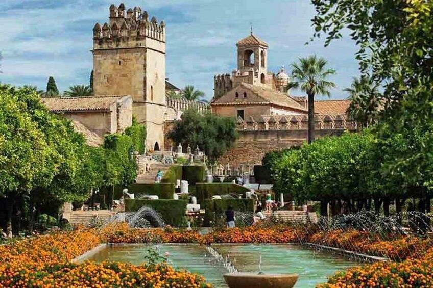 A historic castle with a tower, a fountain, and a garden with orange flowers. 4