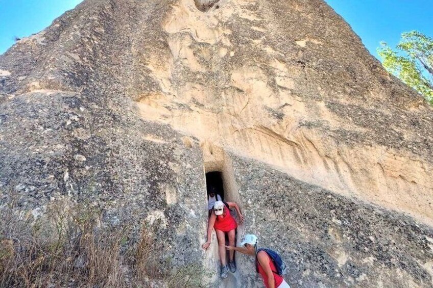 A large rock formation with a cave entrance, a person in red, and another person in a blue shirt. 2