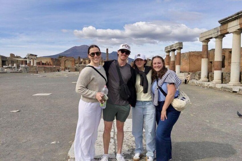 Un gruppo di persone in piedi di fronte a rovine antiche con colonne e una montagna sullo sfondo. 2
